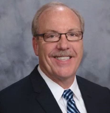 A man in glasses and suit standing next to wall.